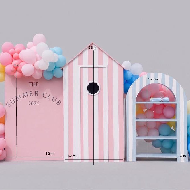 Pink and white striped beach hut with 'The Summer Club 2026' branding, surrounded by colorful balloons.